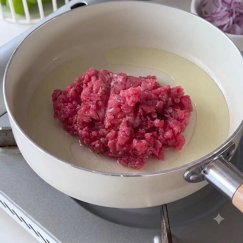 熱した白いフライパンに生の牛ひき肉を入れている様子。