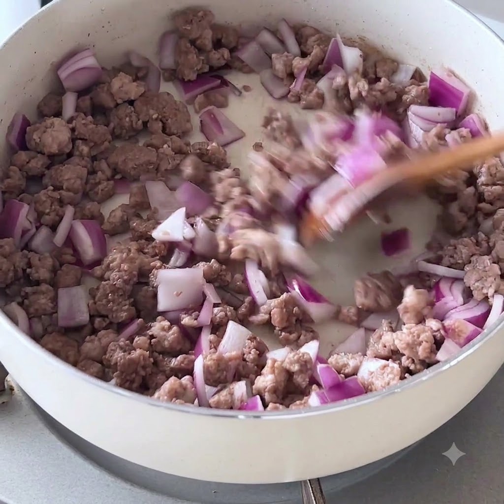 木べらで白いフライパンの中の紫玉ねぎと炒めた牛ひき肉を混ぜている様子。
