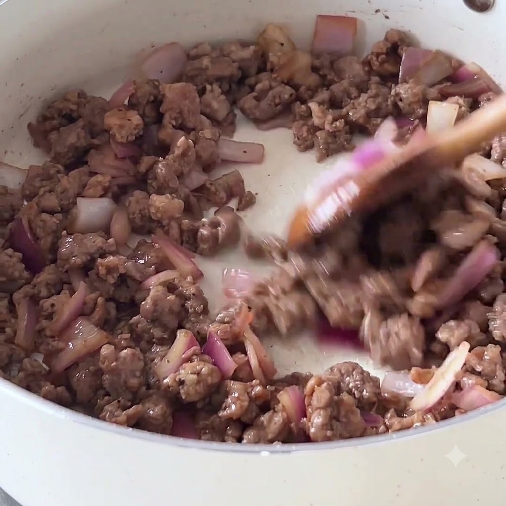 木べらで牛ひき肉と紫玉ねぎを白いフライパンで炒めている様子。