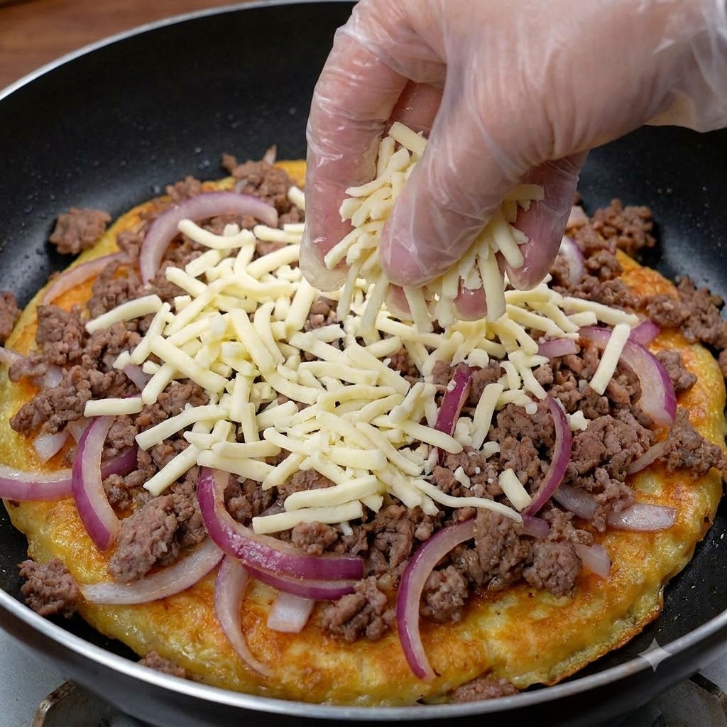 牛肉と玉ねぎの上にたっぷりの細切りチーズを手袋をした手で振りかけている様子。