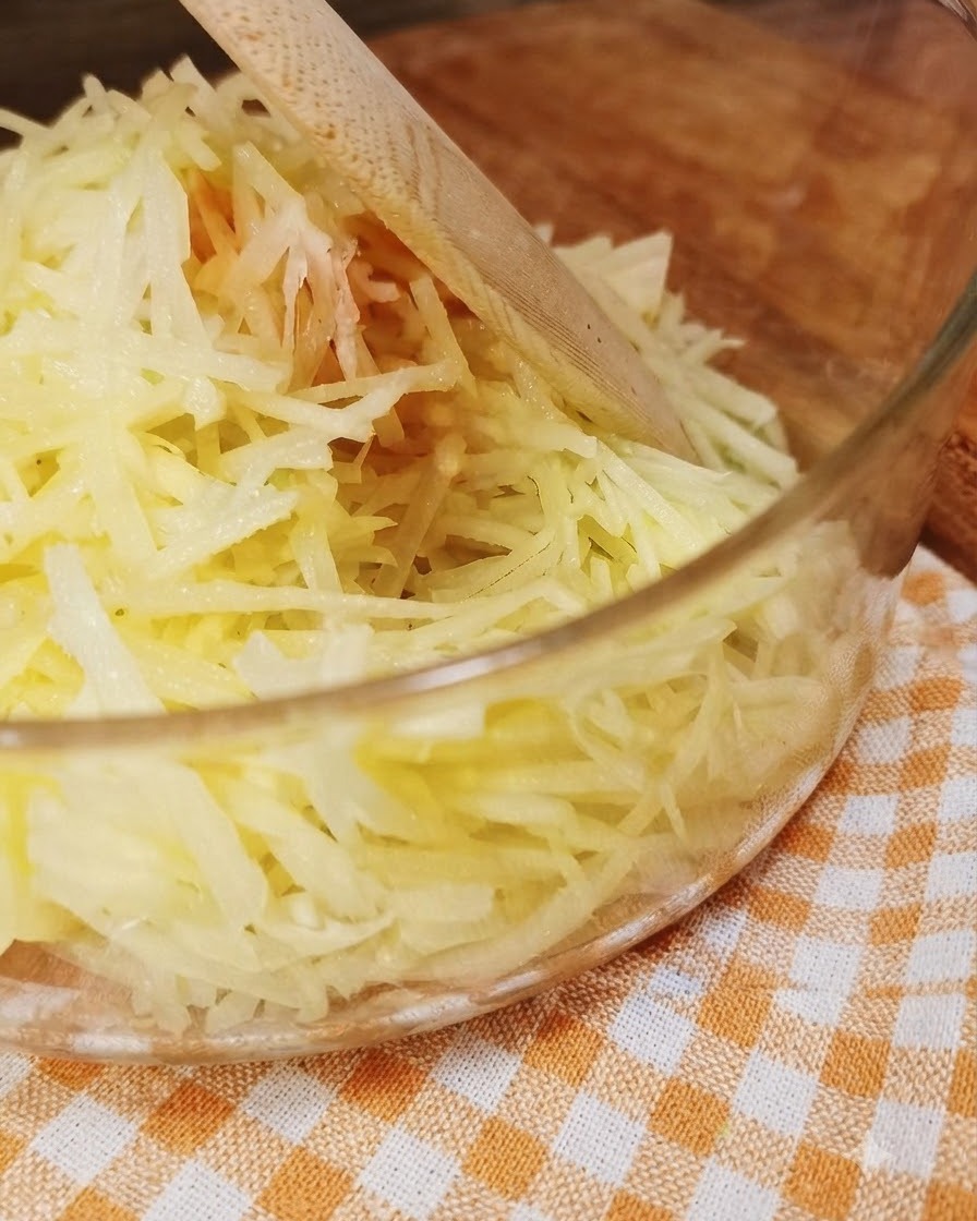 木製の調理器具が添えられた、透明なガラスボウルの中の新鮮な千切りじゃがいも