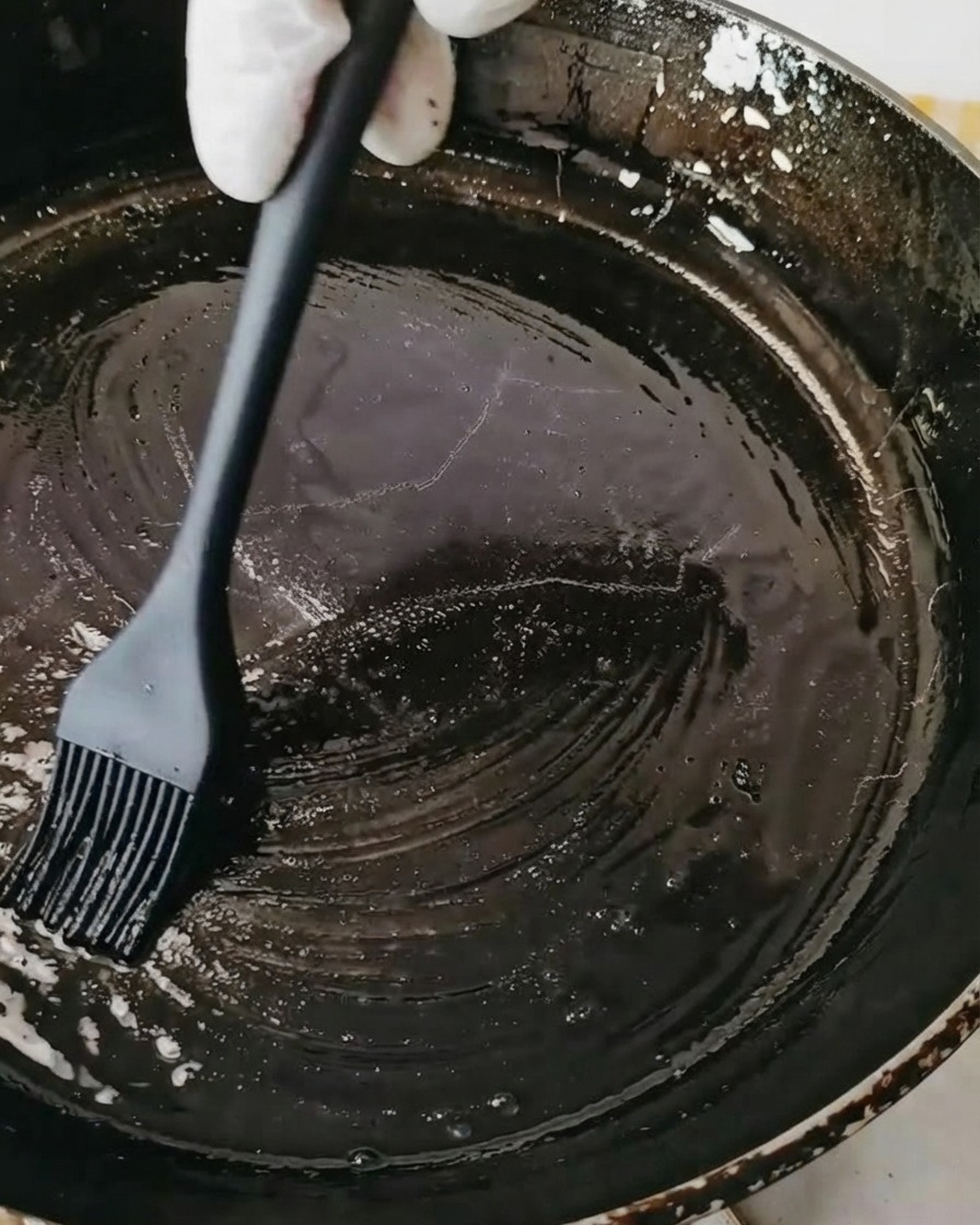 黒いシリコン製のペストリーブラシを使って、黒いスキレットに油を塗っている様子