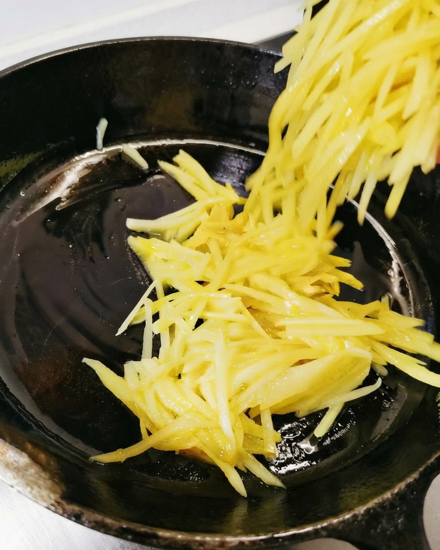 油を引いた黒いスキレットに千切りじゃがいもを流し入れて広げているところ