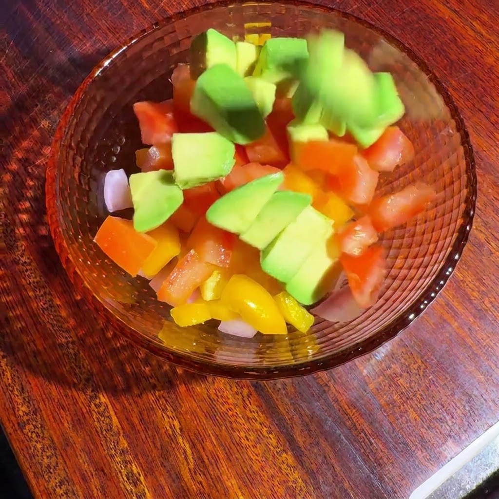 ガラスボウルに入った角切り野菜とアボカドをドレッシングで和えている様子。