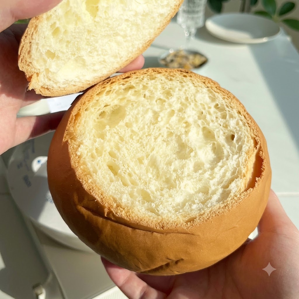 上部のフタ部分を取り外した、中をくり抜いた丸いパンのローフを手に持っている様子。