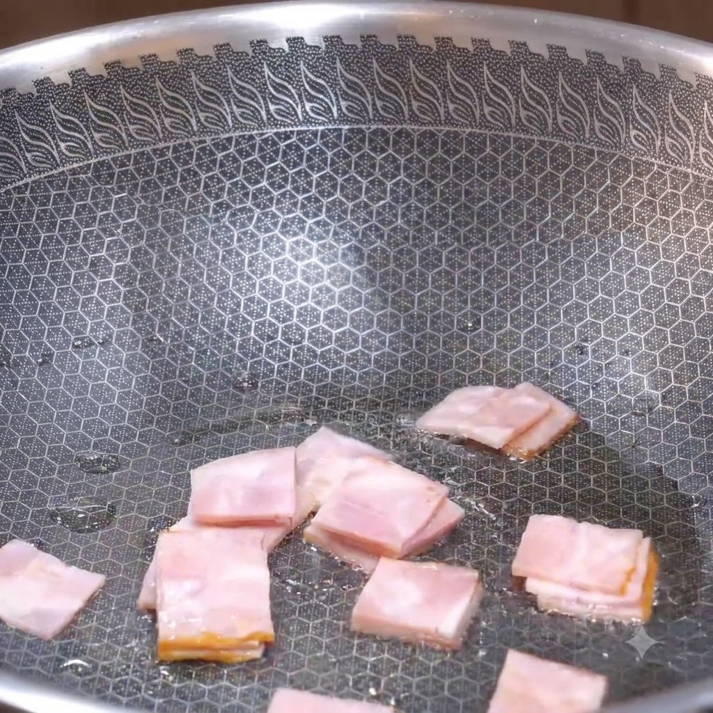 四角く切ったベーコンのピースが、テクスチャーのある中華鍋の中で焼き色がつき始めるまでフライパンで炒められている様子。