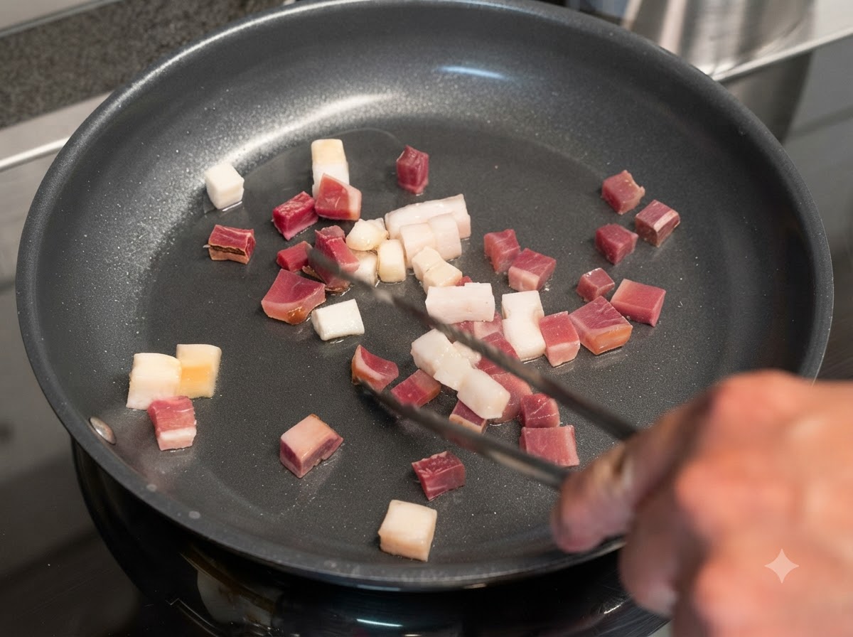 フライパンでサイコロ状のベーコンと塩漬け肉がジューシーに炒められており、トングで返されているところ。