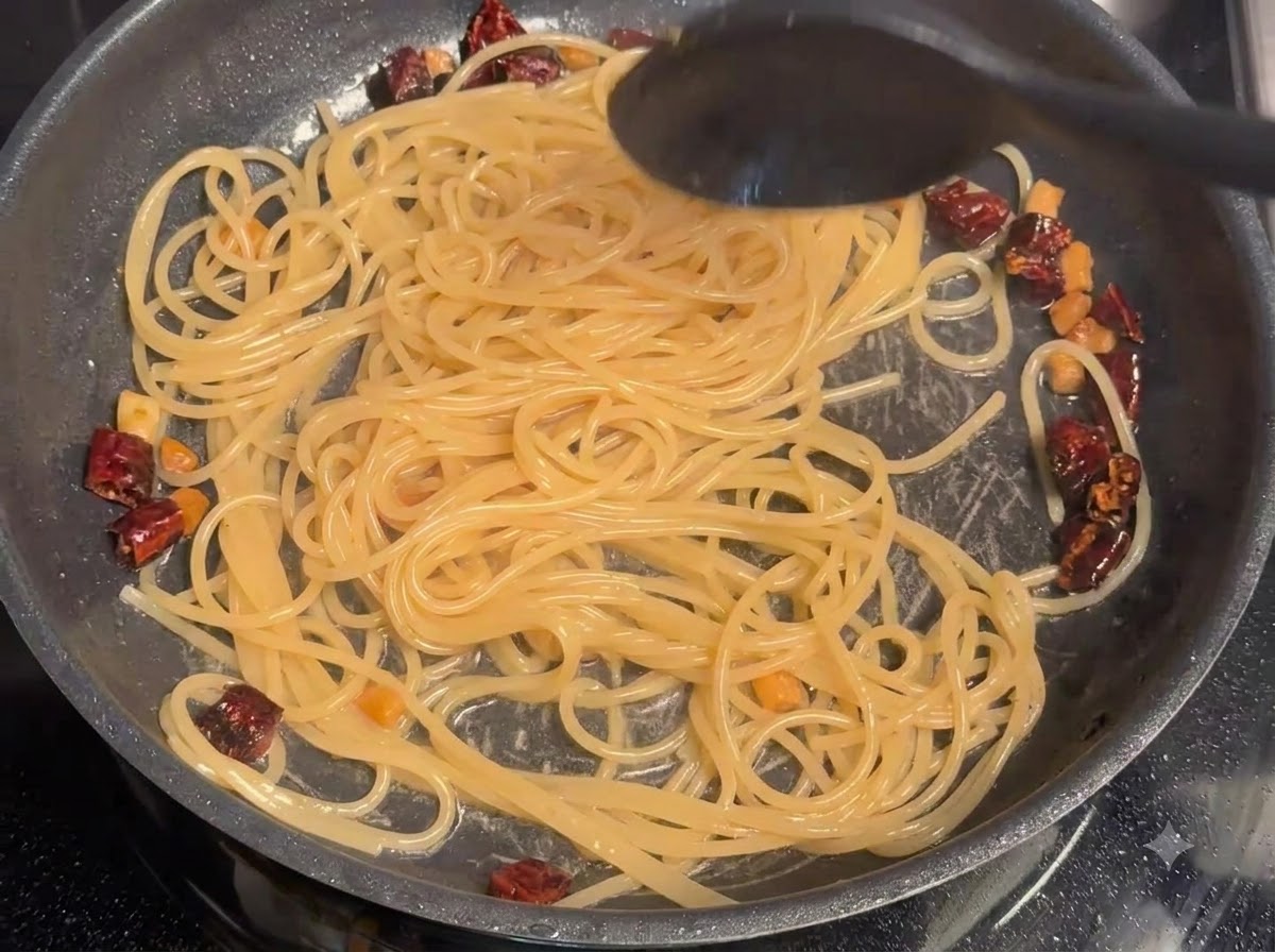 フライパンの中でスパゲッティと豚肉に茹で汁が混ぜ合わされているところ。