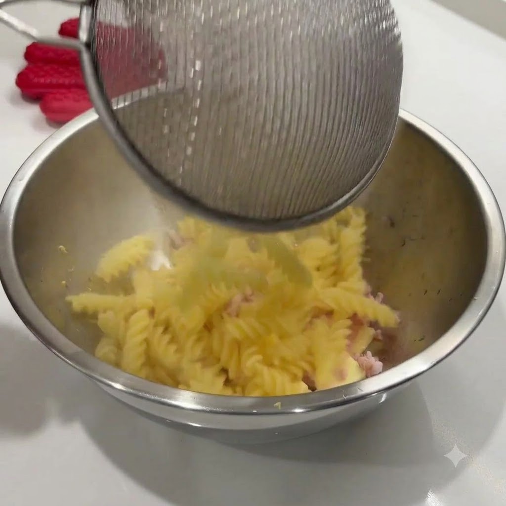 茹で上がったスパイラルパスタを、網じゃくしからソースの材料が入ったボウルに移している様子