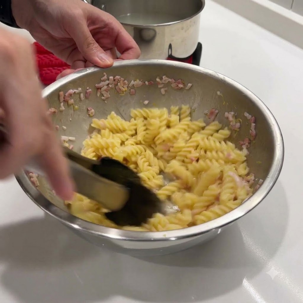 トングを使って、熱いパスタとバターの混合物をボウルの中で混ぜている様子