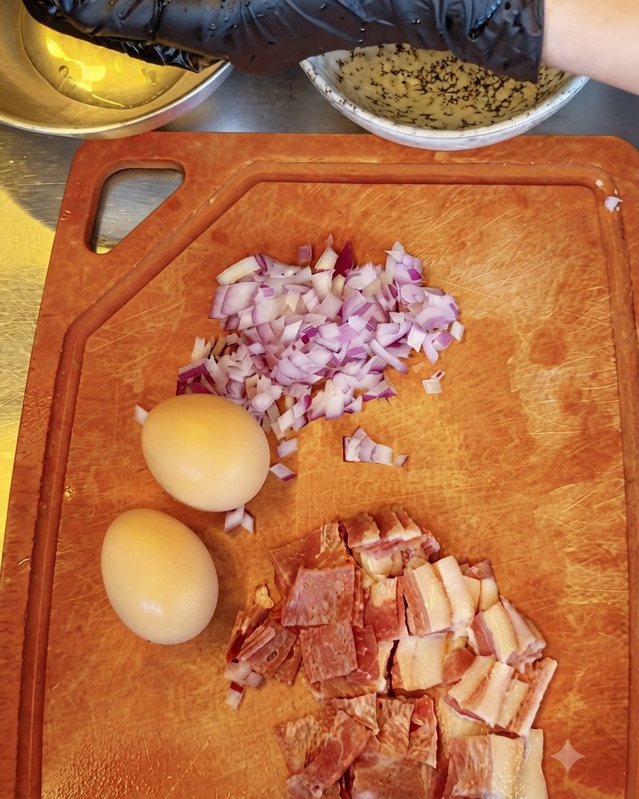手袋をつけた手で卵黄を分け、他の食材が置かれたまな板のそばでボウルにかざしている様子。