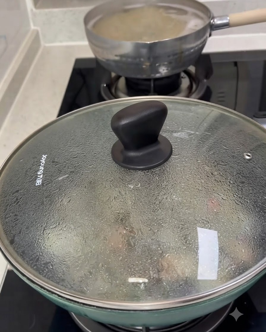 調理中のアサリが入ったフライパンにガラスの蓋が被せられ、表面に水滴の結露が見える様子。