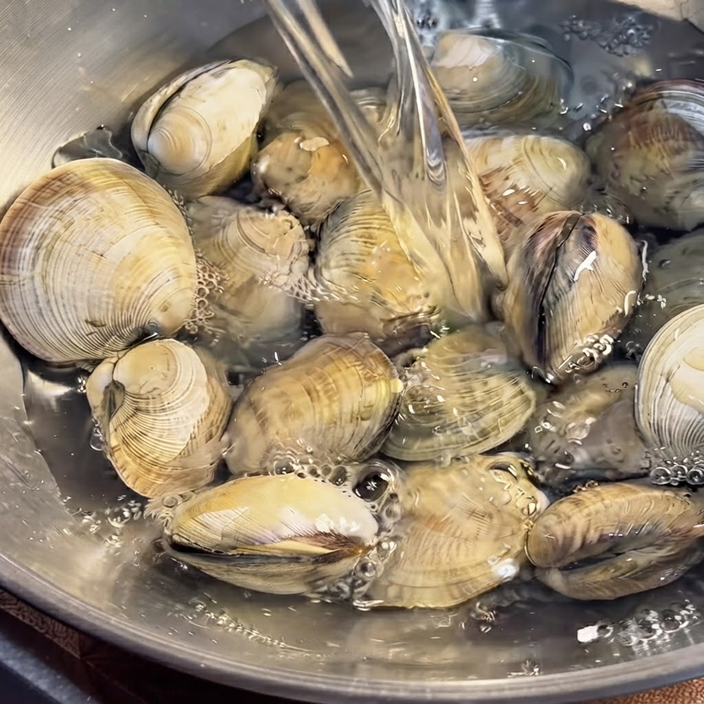 ボウルの水に浸されたアサリを、手でしっかりと洗浄している様子。