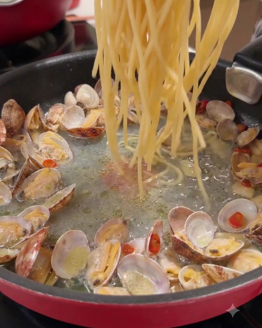 調理済みのあさりとうま味スープが入ったフライパンに、ロングパスタが投入されている様子。