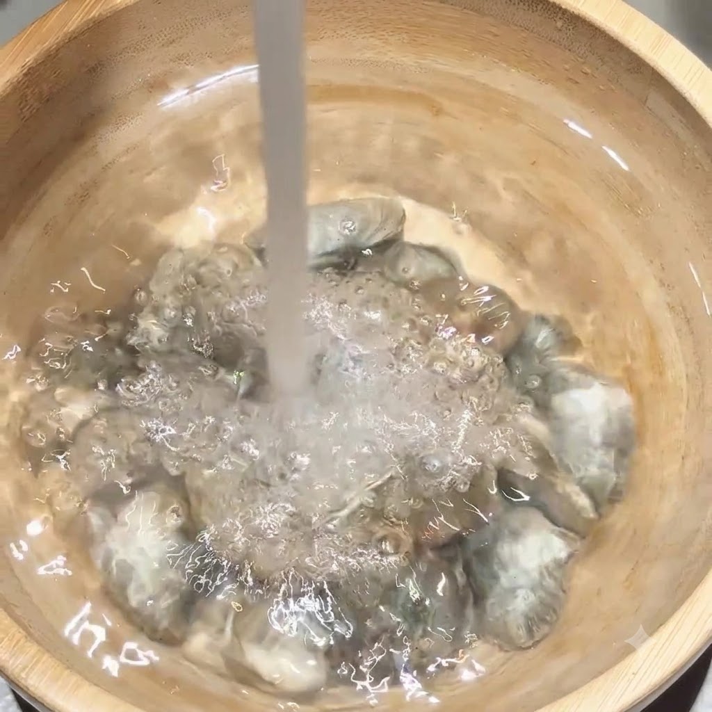 木製のボウルに入ったアサリに、水道水が直接注がれている様子。