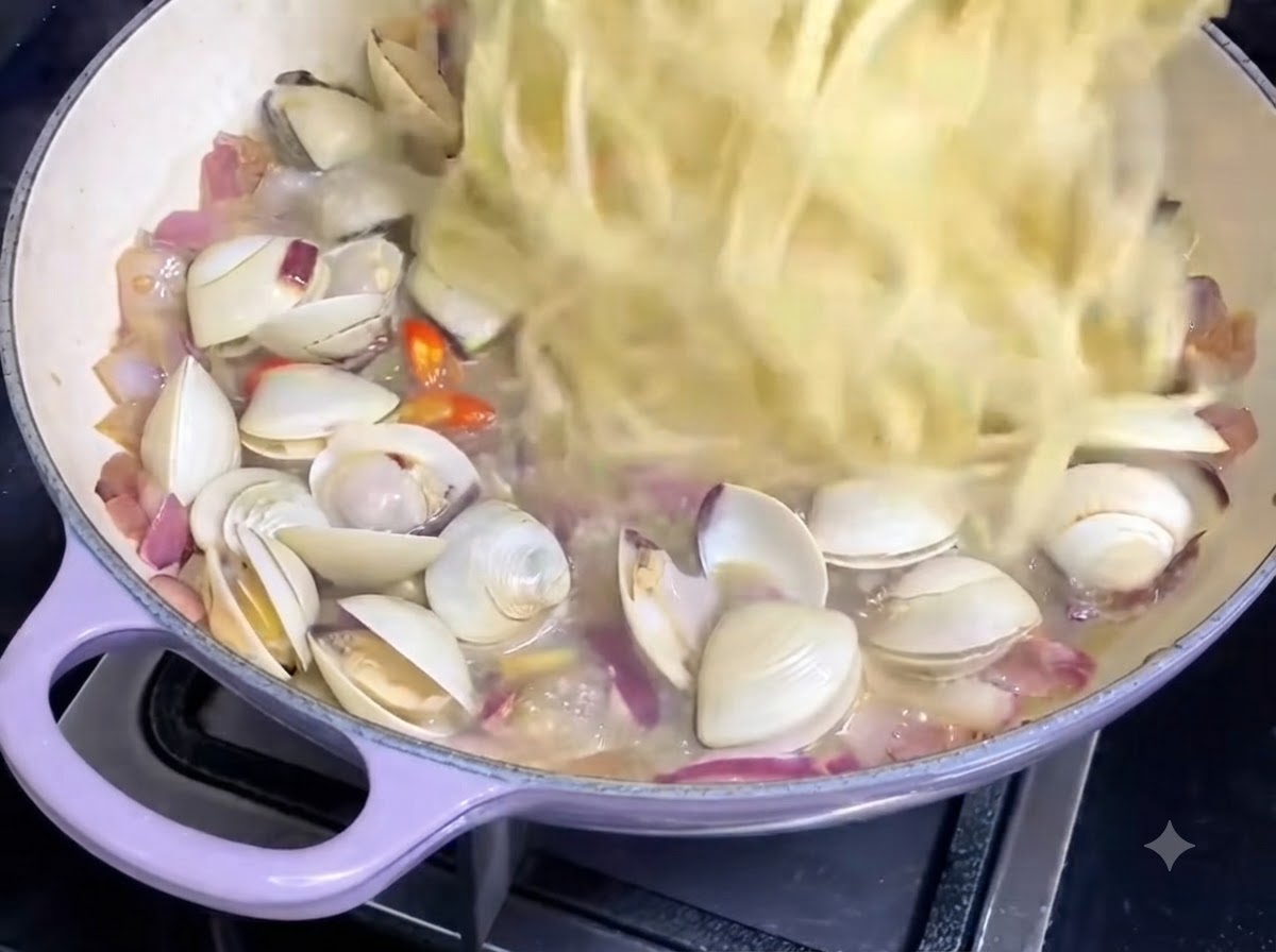 アサリソースと玉ねぎの入ったフライパンに、茹でたスパゲッティの麺が投入されている様子。