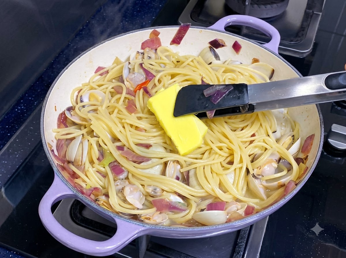 スパゲッティとアサリが混ざったフライパンの中で、黄色いバターのかたまりが溶けている様子。