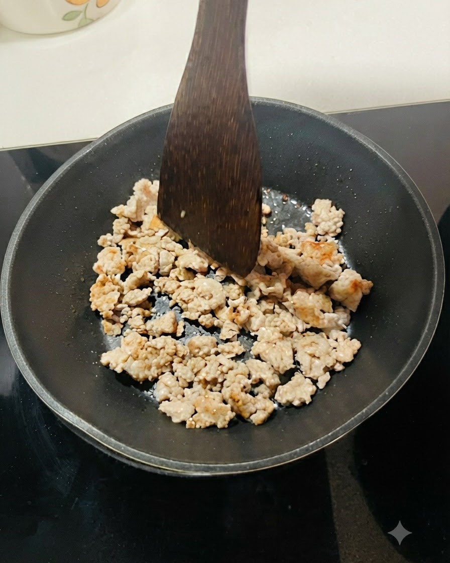 黒いフライパンの中でひき肉が炒められ、木製のヘラで細かくほぐされている様子。