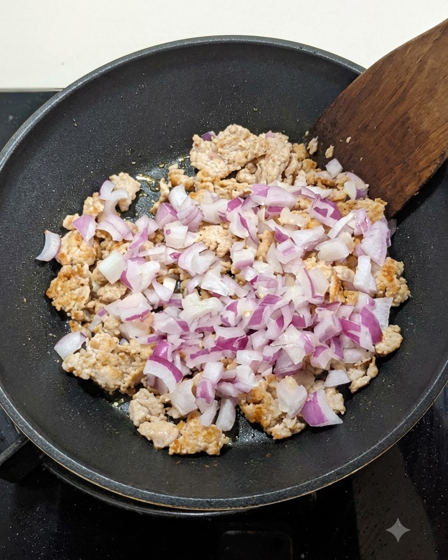 フライパンの中で軽く炒めたひき肉にみじん切りの赤玉ねぎが加えられ、木べらで混ぜ合わされている様子。