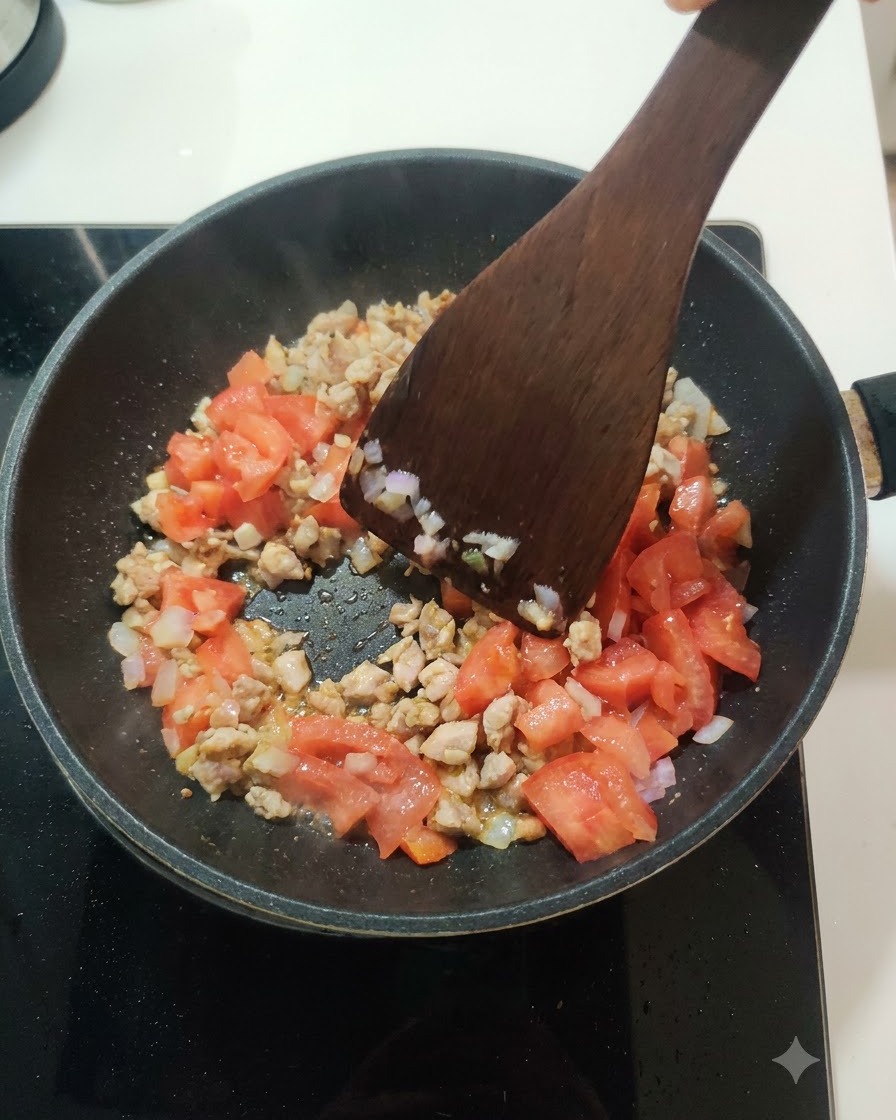 フライパンの中の肉と玉ねぎの混合物に、フレッシュな角切りトマトが加えられている様子。
