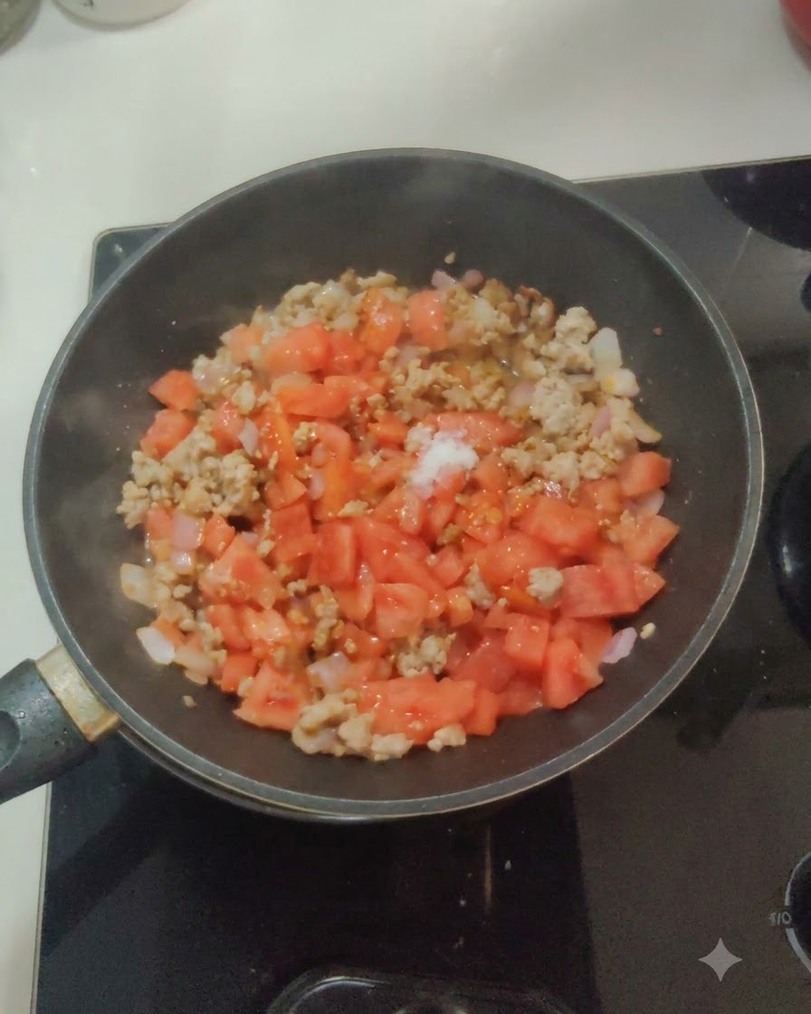 フライパンのトマト、玉ねぎ、肉の混合物の上に、白い塩と砂糖が振りかけられている様子。