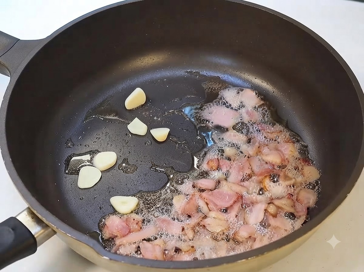 フライパンでスライスしたニンニクとベーコンが一緒に炒められている様子。