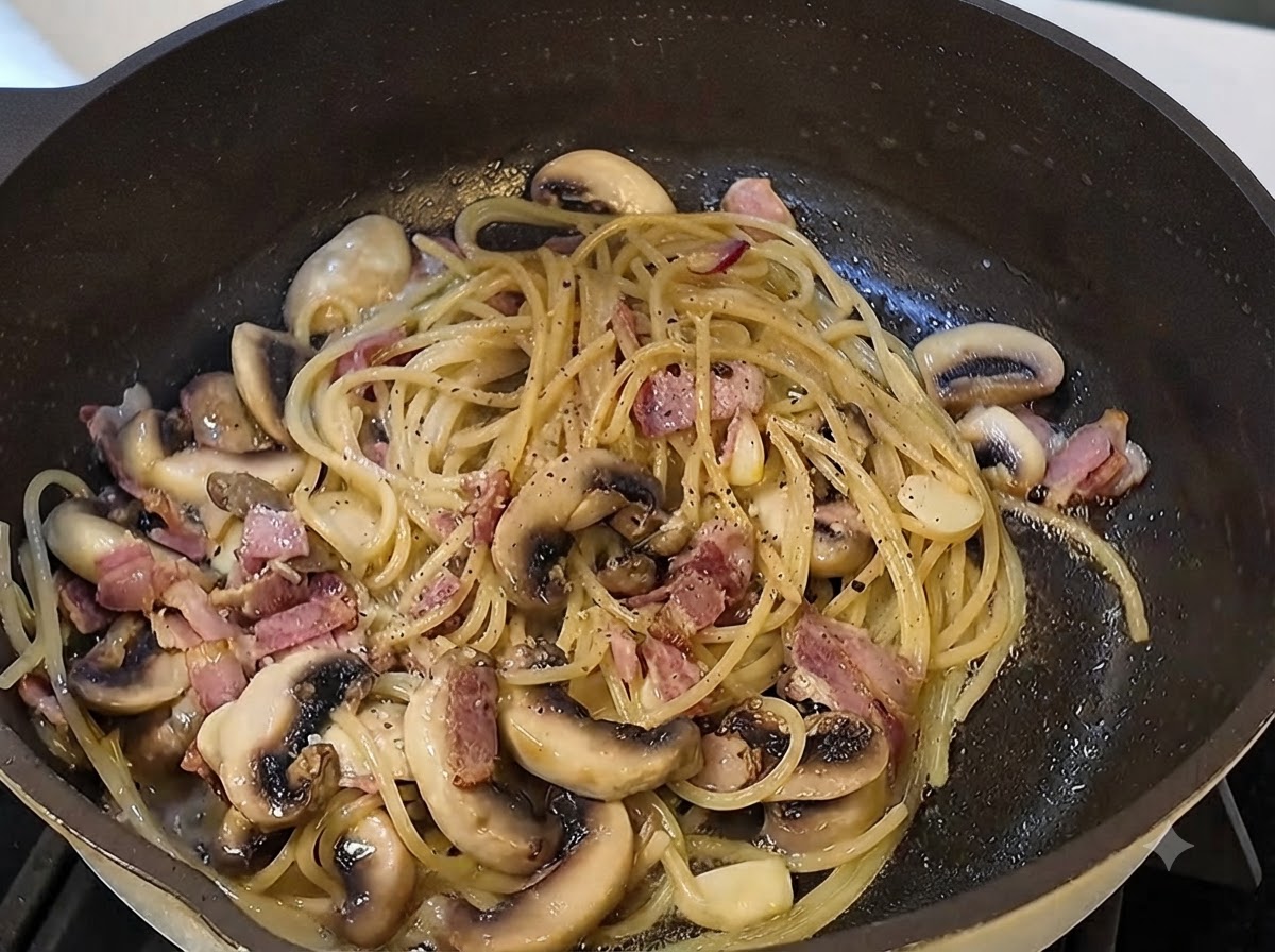 パスタの入ったフライパンに黒トリュフソースと挽きたての黒こしょうが加えられている様子。