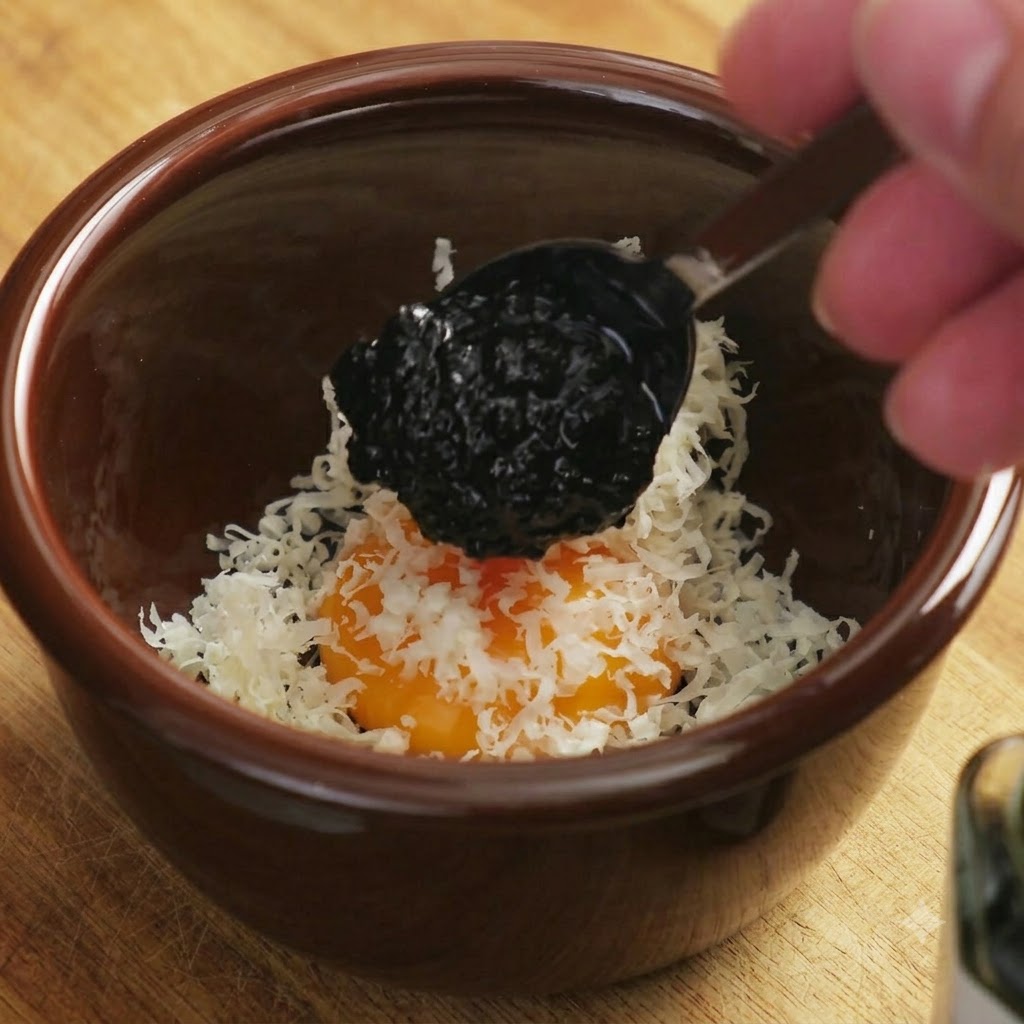 スプーンですくった黒い黒トリュフソースが、卵黄とチーズの混合物に落とされる瞬間。