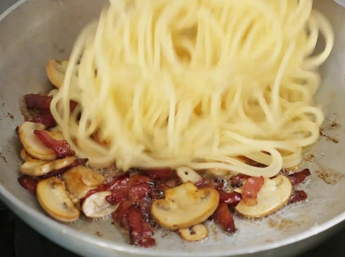茹で上がったスパゲッティが、具材の入ったフライパンの中に投入されている様子。