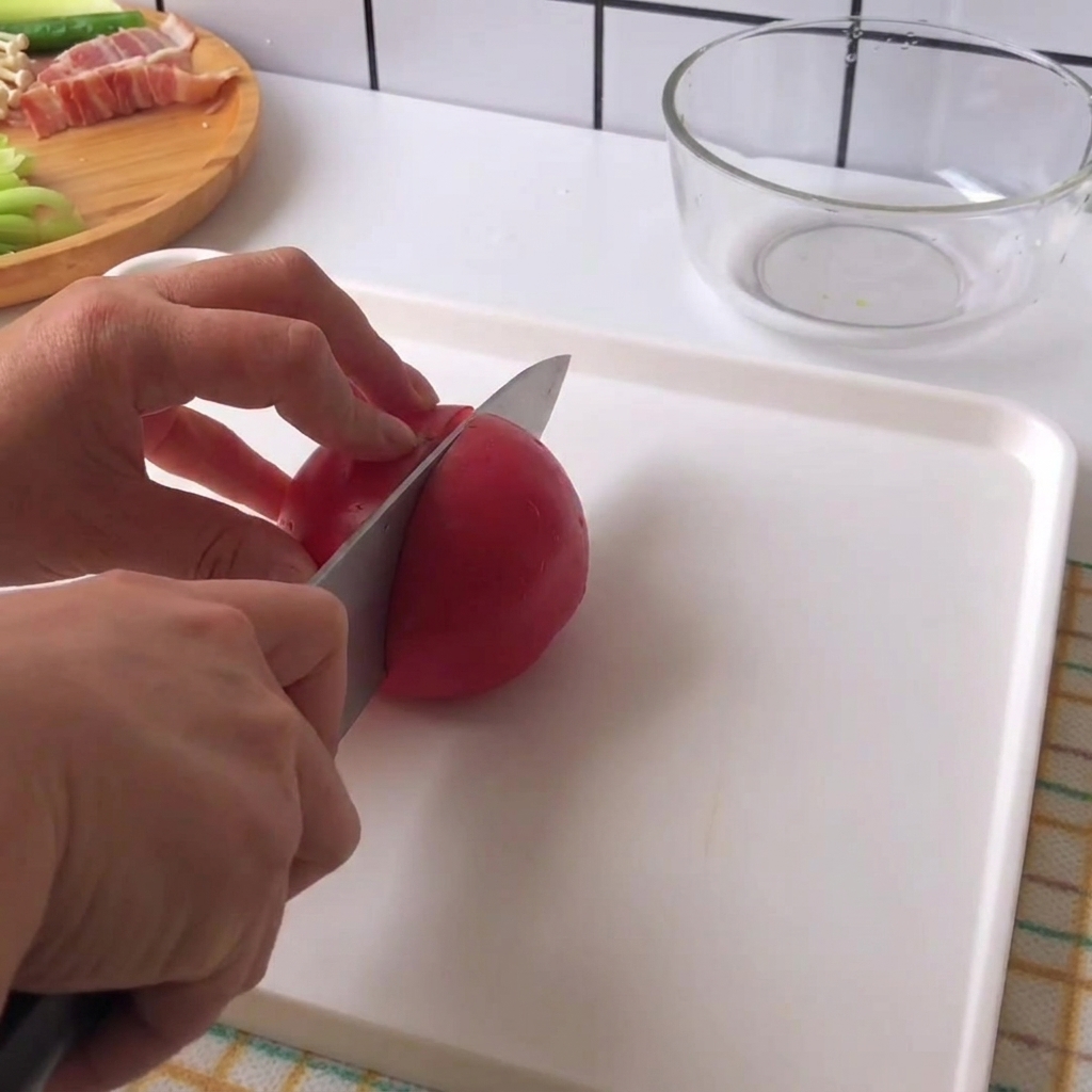 白いまな板の上で、包丁を使って赤いフレッシュトマトを一口大にスライスしている手。