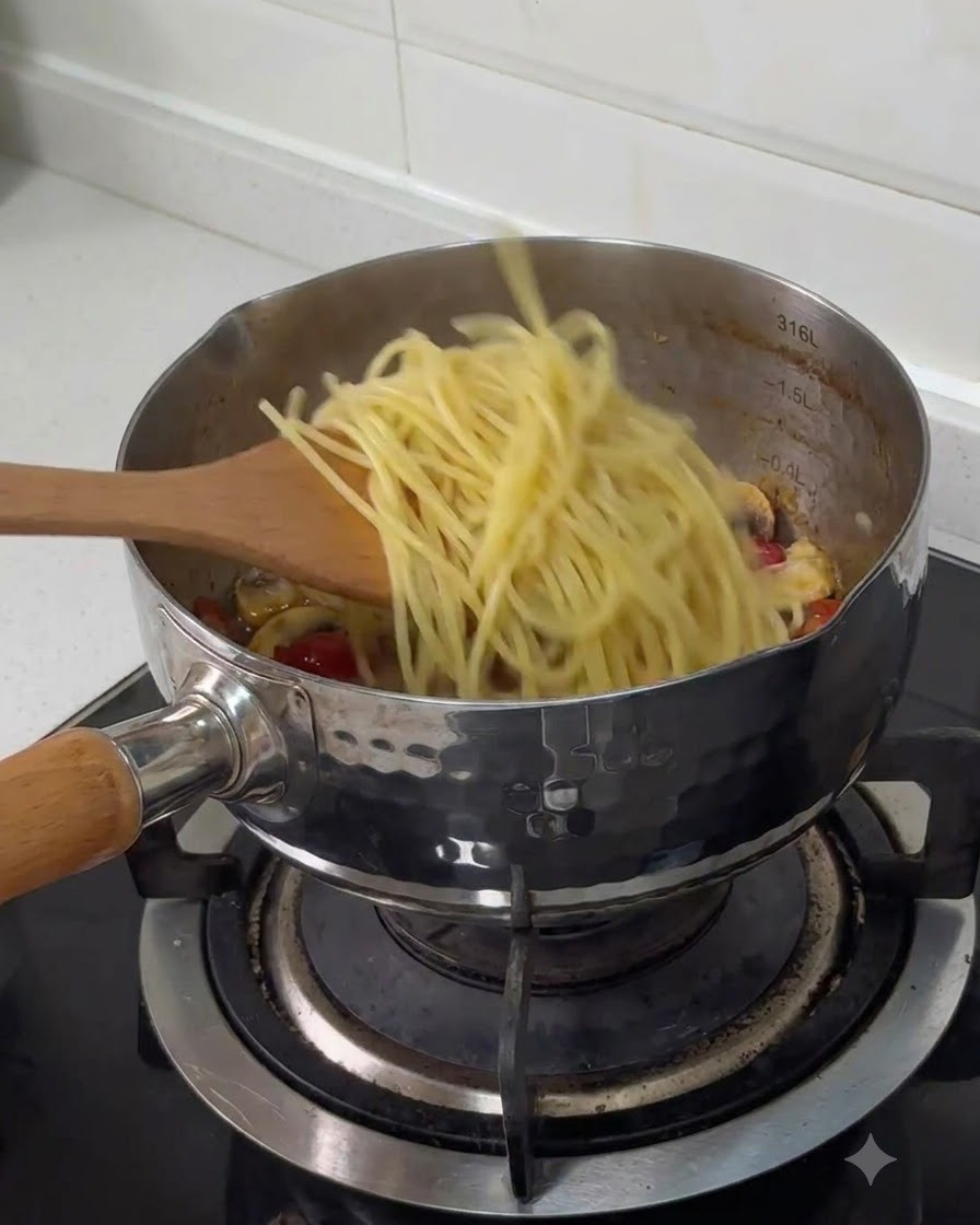 木べらを使って、茹でたスパゲッティを他の調理済み具材が入ったステンレス製の鍋に移している様子。