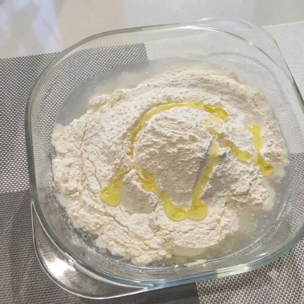 ガラスボウルの中の小麦粉と水の上にオリーブオイルがかけられている様子。