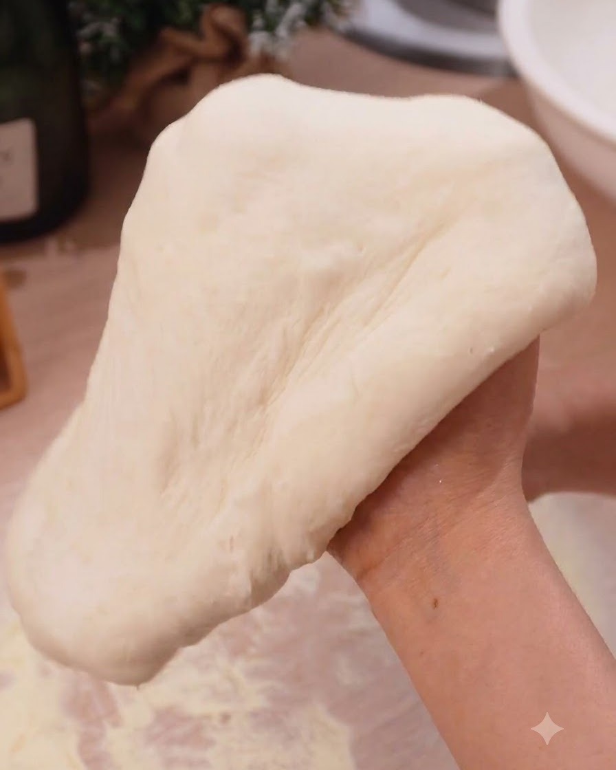 キッチンで両手を使ってピザ生地を滑らかに伸ばしている様子