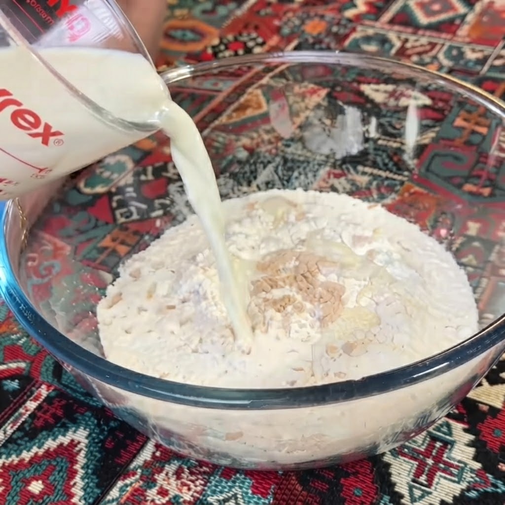 透明な計量カップから、小麦粉とイーストが入ったボウルに牛乳を注いでいる様子。