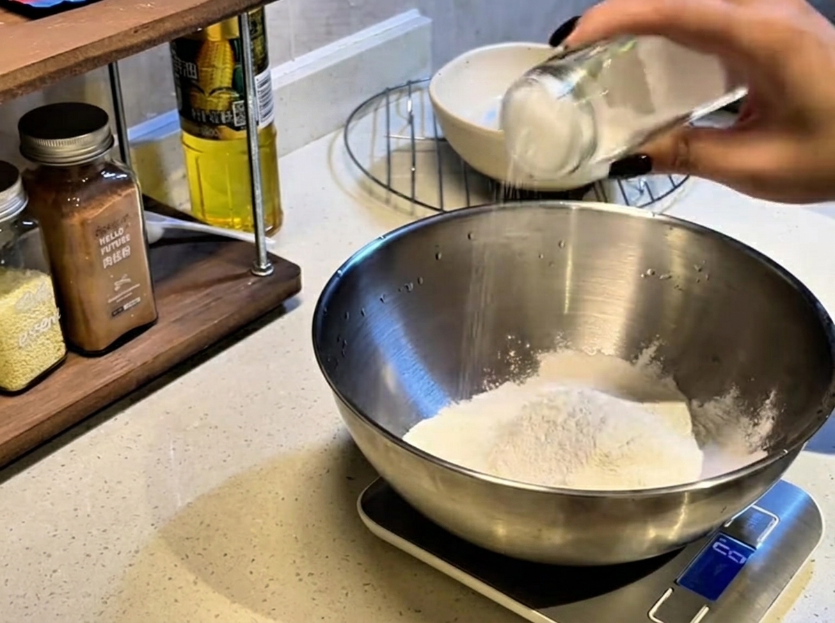 大きなボウルに入った小麦粉に塩を振り入れている様子。