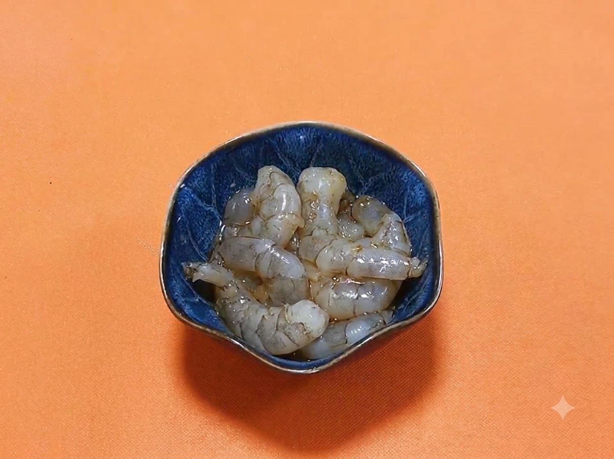ダークソイソースとスパイスの光沢のあるマリネ液が入った濃い青色のボウルに盛られた、殻をむいた生のエビ。
