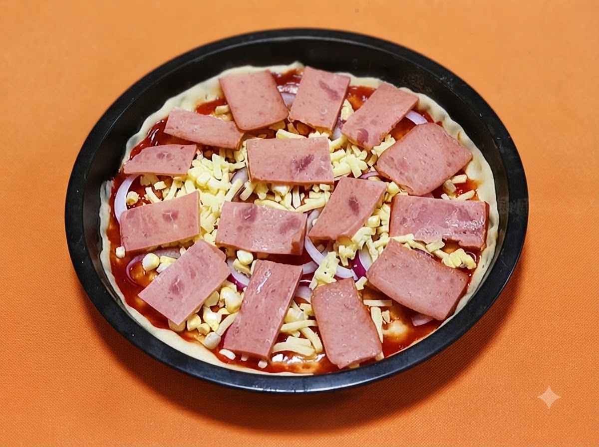 チーズとタマネギをトッピングしたピザクラストの上に、ピンク色の四角いハムのスライスが規則正しく並べられている様子。