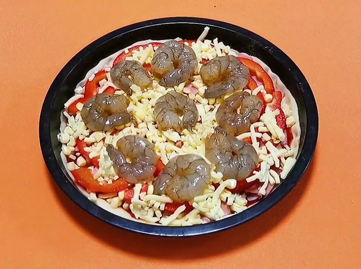 チーズ、パプリカ、ハムが乗ったピザの上に、生のマリネエビが円形に並べられている様子。
