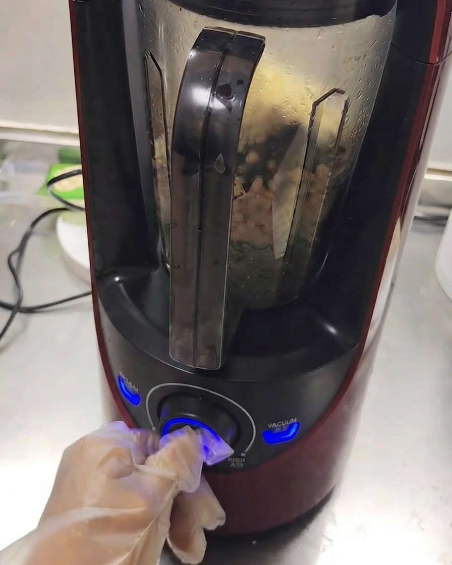 手がダイヤルを回している間、内部で材料が混ざり合っている稼働中のブレンダー。
