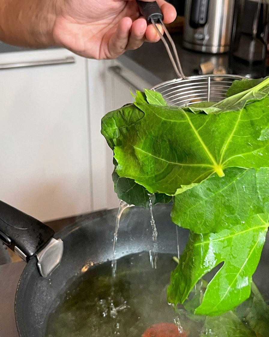 沸騰した鍋の水から、ワイヤーのストレーナーで茹でたての青菜を引き上げている様子。