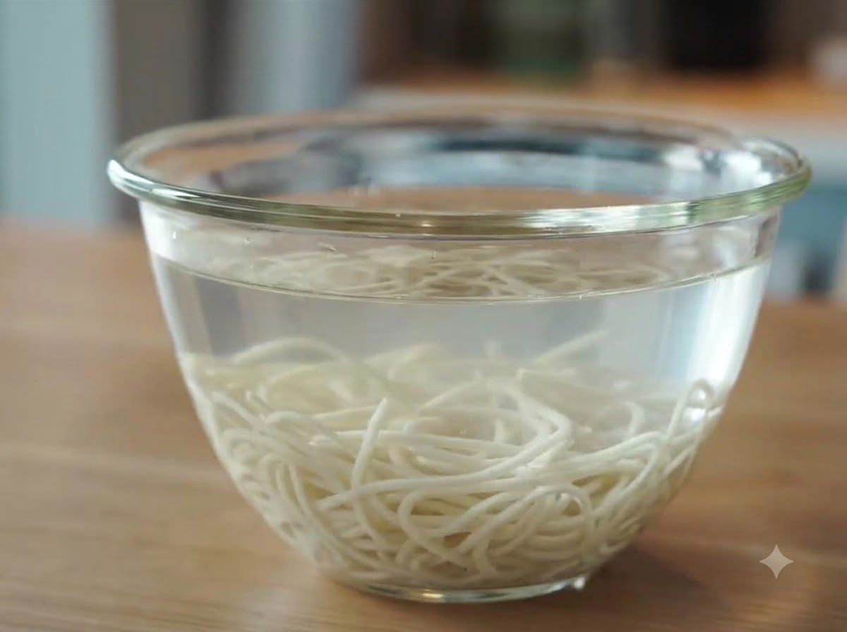 茹で上がったばかりのラーメンの麺を、冷水を入れたガラスボウルに浸して冷やしている様子。