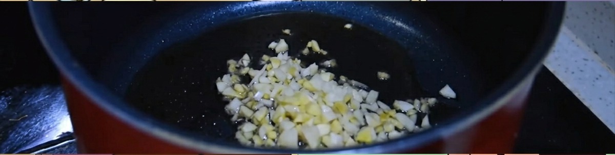 熱せられたごま油が入った黒い鍋の中で、おろし生姜とニンニクがジュージューと炒められている様子。
