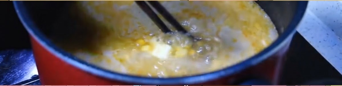 黒い鍋の中で、コーンとバターが入った激しく沸騰するオレンジ色の味噌スープを箸でかき混ぜている様子。