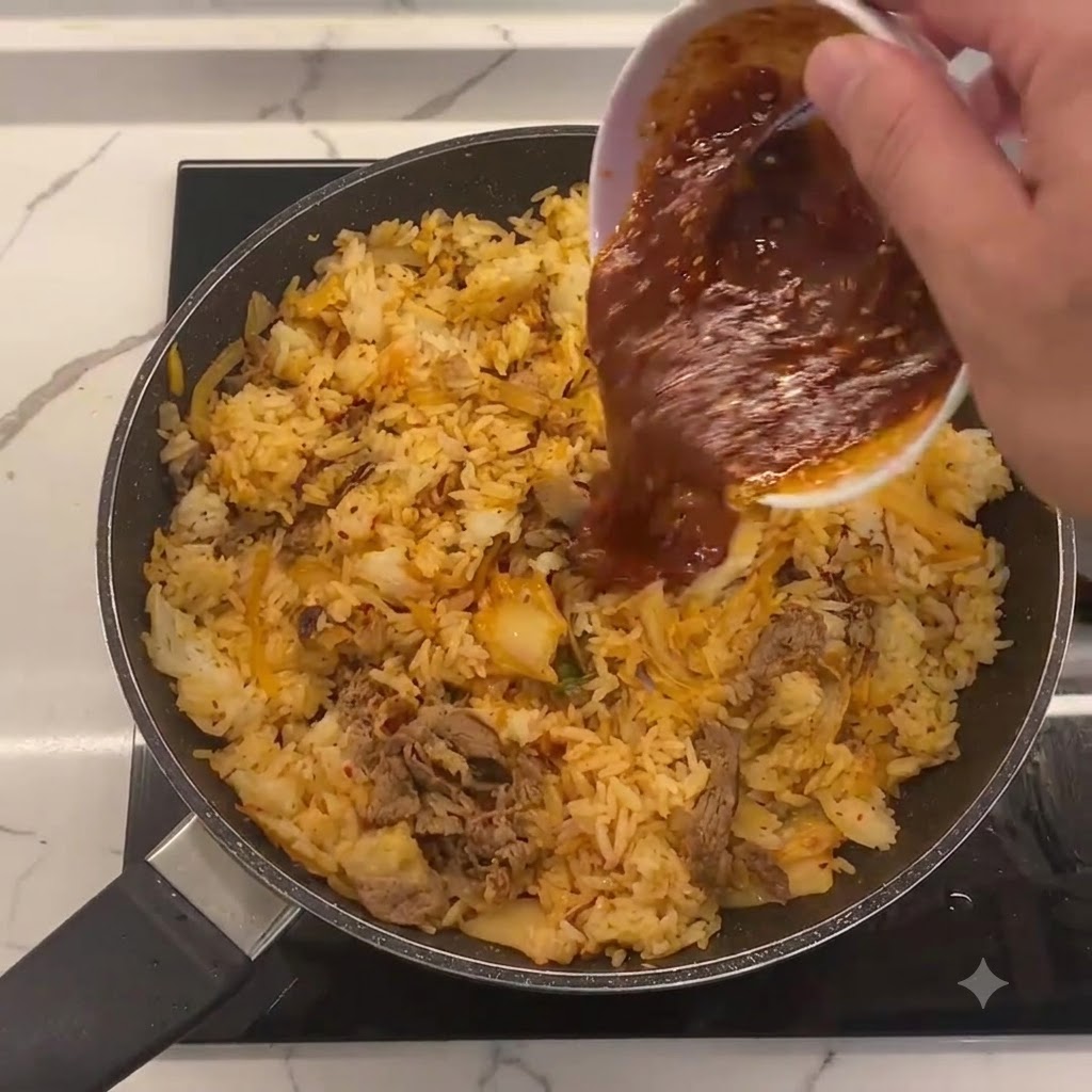 フライパンの中央のチャーハン、キムチ、牛肉に向けて白い小鉢から注がれる特製ソース