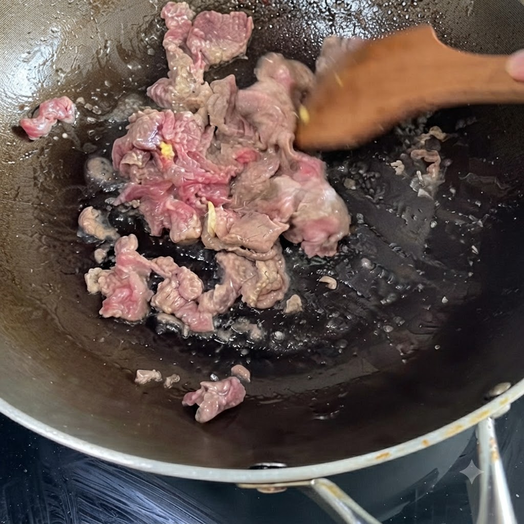 熱した中華鍋の中で、木べらを使ってジュージューと炒められている下味付きの牛肉。