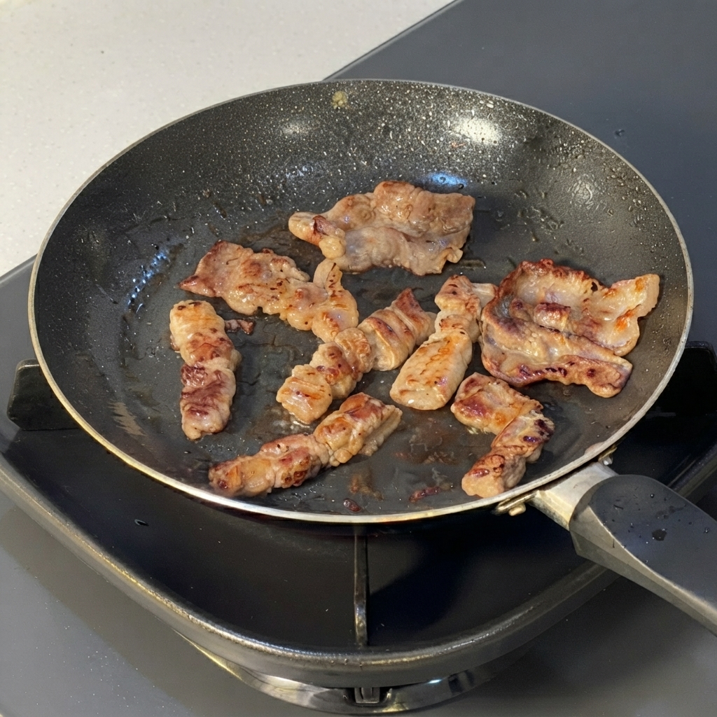 フライパンの中で、キッチンバサミを使って小さく切り分けられている調理済みの牛肉のスライス。