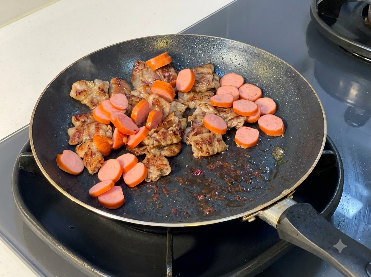調理済みの牛肉スライスが入ったフライパンに加えられている、スライスされたソーセージ。