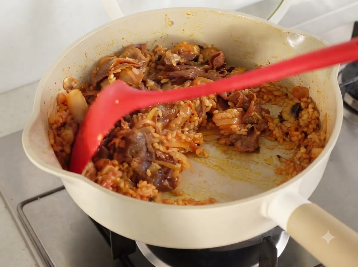 フライパンの中で、すべての具材とご飯をキムチの汁が全体に行き渡るようによく炒め合わせている様子。