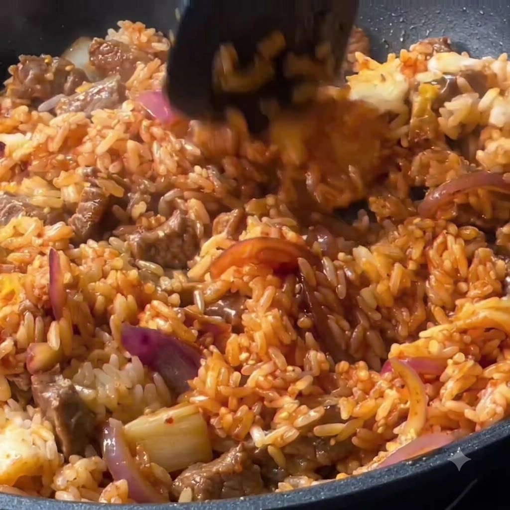 フライパンの中で、ご飯、牛肉、野菜がスパチュラを使ってしっかりと混ぜ合わされている様子。