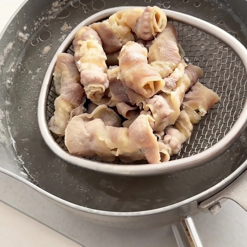 ワイヤー製のストレーナーで下茹でした牛肉ロールを熱いお湯の鍋から引き上げているところ。